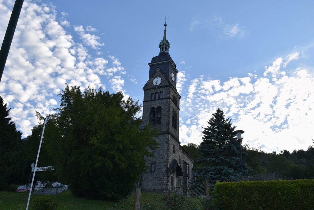 Kirchturm vor blauem Himmel und wenigen Wolken im Hintergrund.