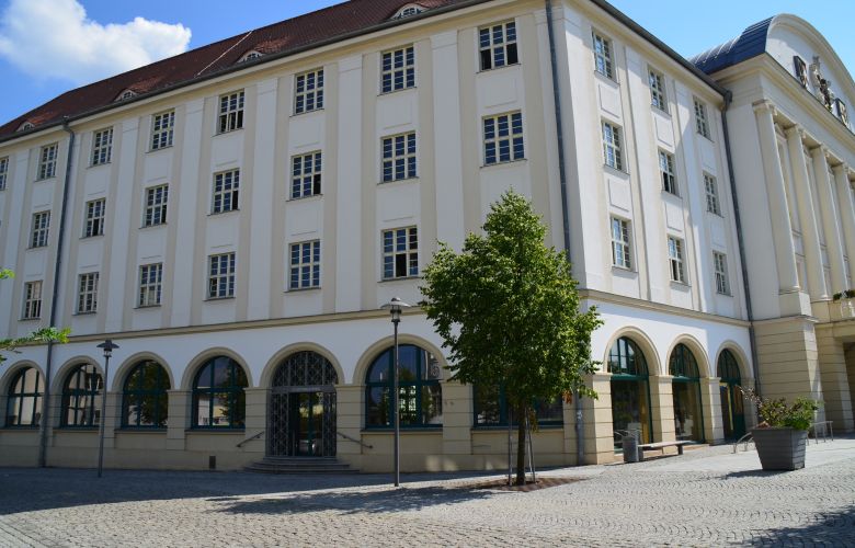 Vierstöckiges helles Gebäude mit Eingangstür zur Stadtbibliothek. Im Vordergrund eine gepflasterte Fläche.