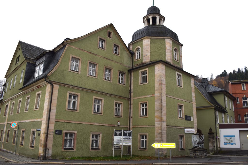 Vierstöckiges grün gestrichenes Gebäude mit einem Turm auf der Rechten Seite.