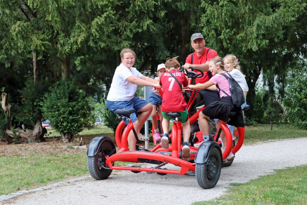 Viele Personen sitzen auf einem Concerencebike und fahren durch einen Park.
