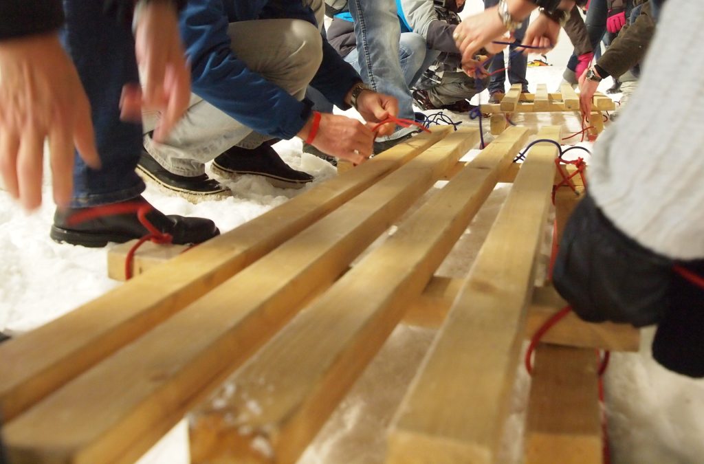 Ein Holzschlitten wird zusammengebaut durch viele Hände.