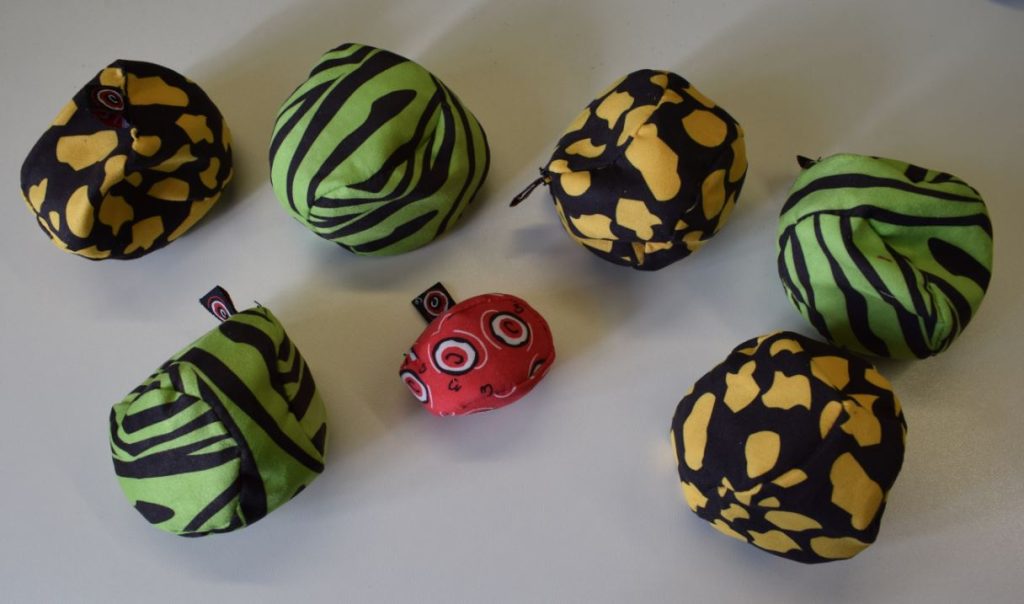 3 grüne Stoffboule, 3 gelbe Stoffboule und ein kleiner rote Stoffsack auf beigem Hintergrund.